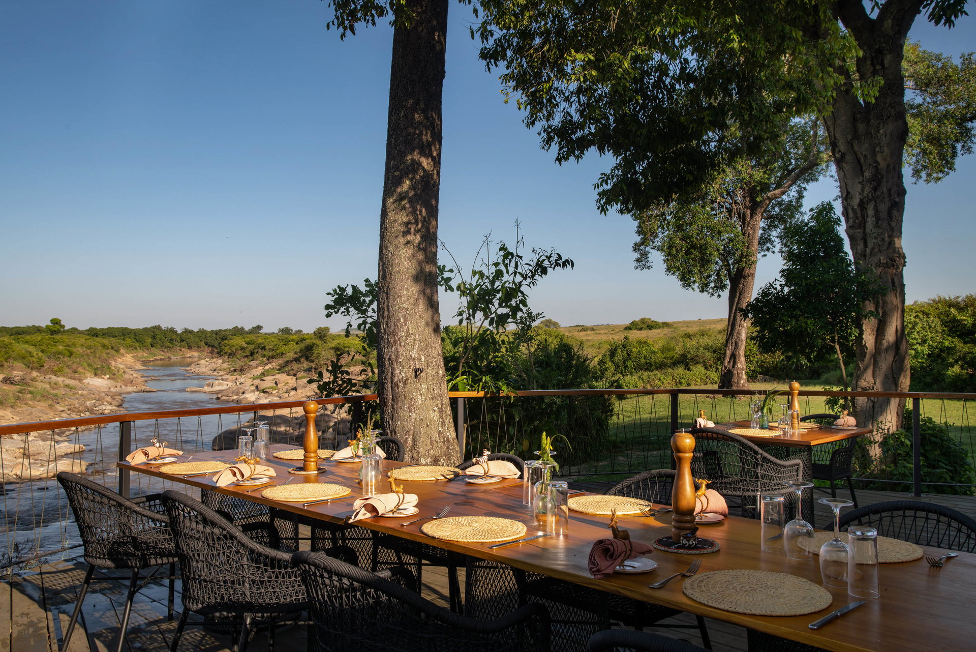 A table laid on the deck at Rekero Camp under the trees by the Talek River