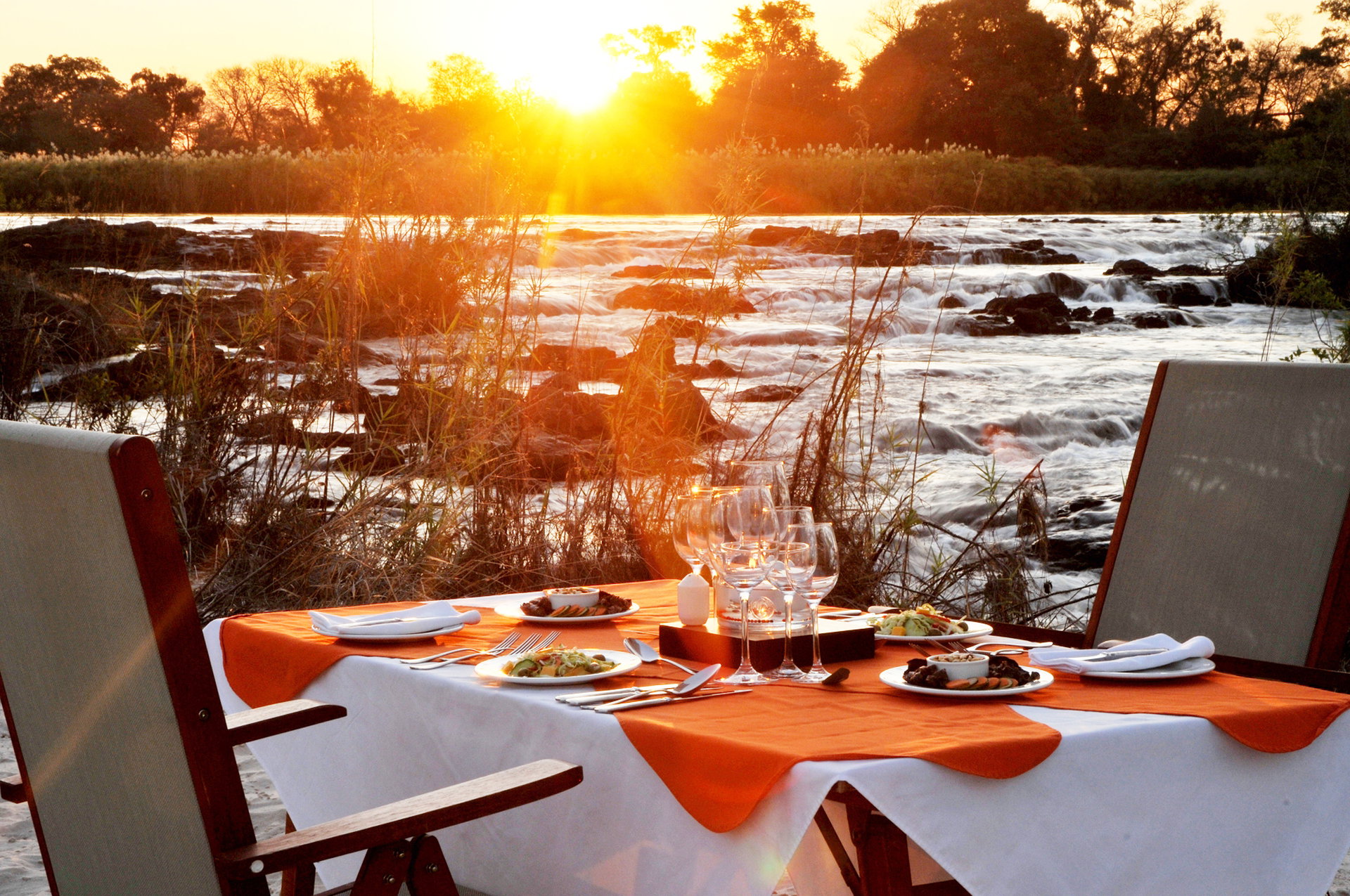 A table set for dinner above the rapids as the sun sets over the Okavango