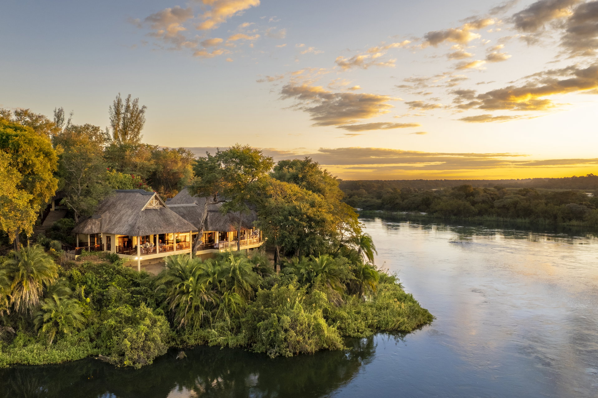 Divava's thatched main building among the trees above the Okavango River at sunset