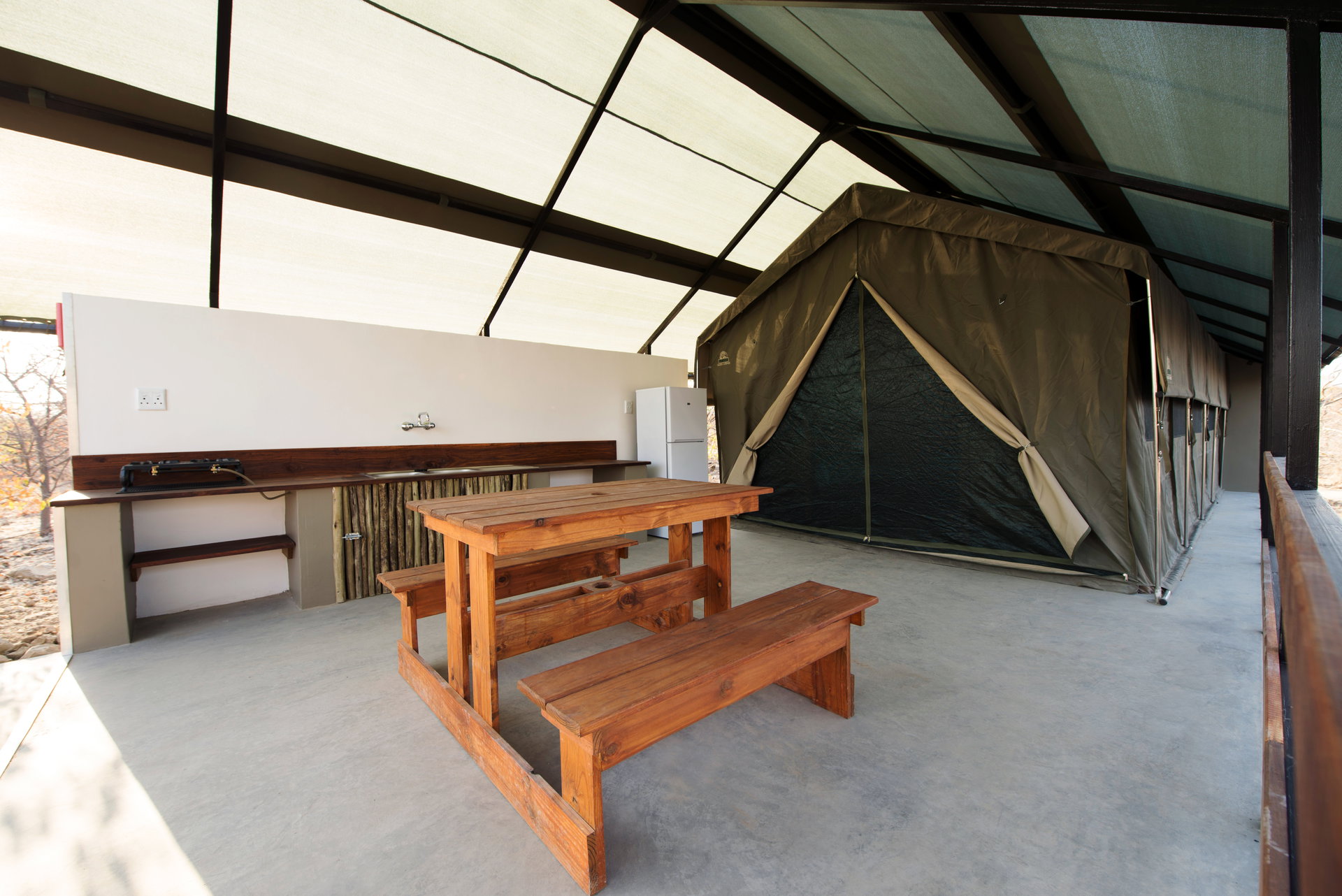 An outdoor kitchen with a table and benches beside a safari tent