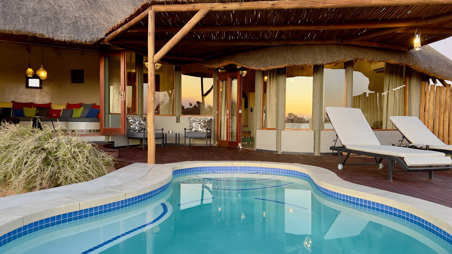 The pool and thatched main building of Kalahari Red Dunes Lodge in the evening light