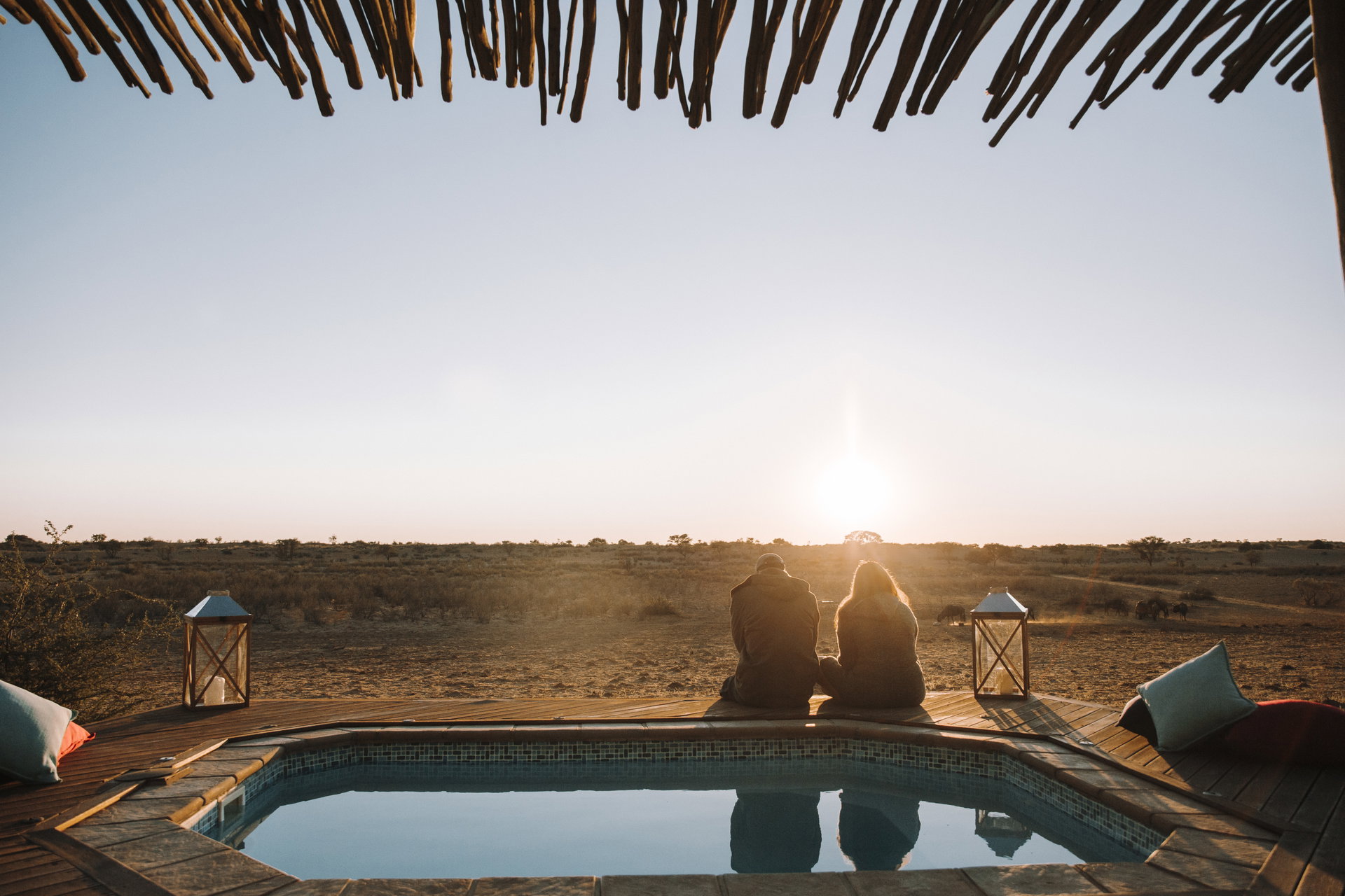 Two guests at the edge of a private pool watching the sun set over the Kalahari