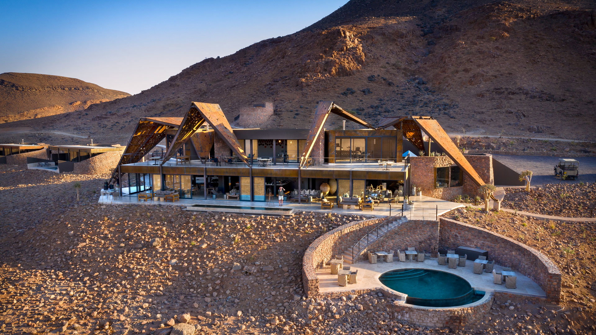 The stone and glass main lodge and pool of andBeyond Sossusvlei Desert Lodge against the mountains