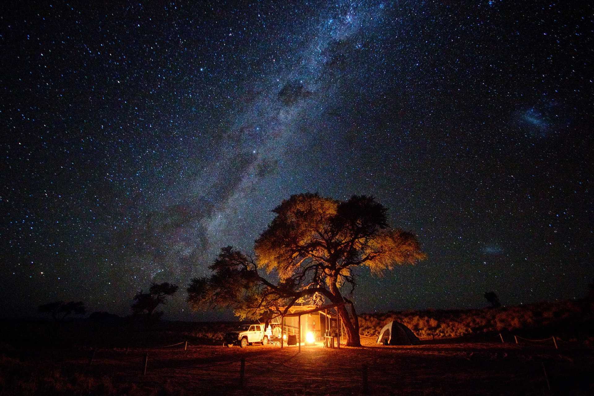 The Milky Way over a campfire and a camelthorn tree in the NamibRand reserve