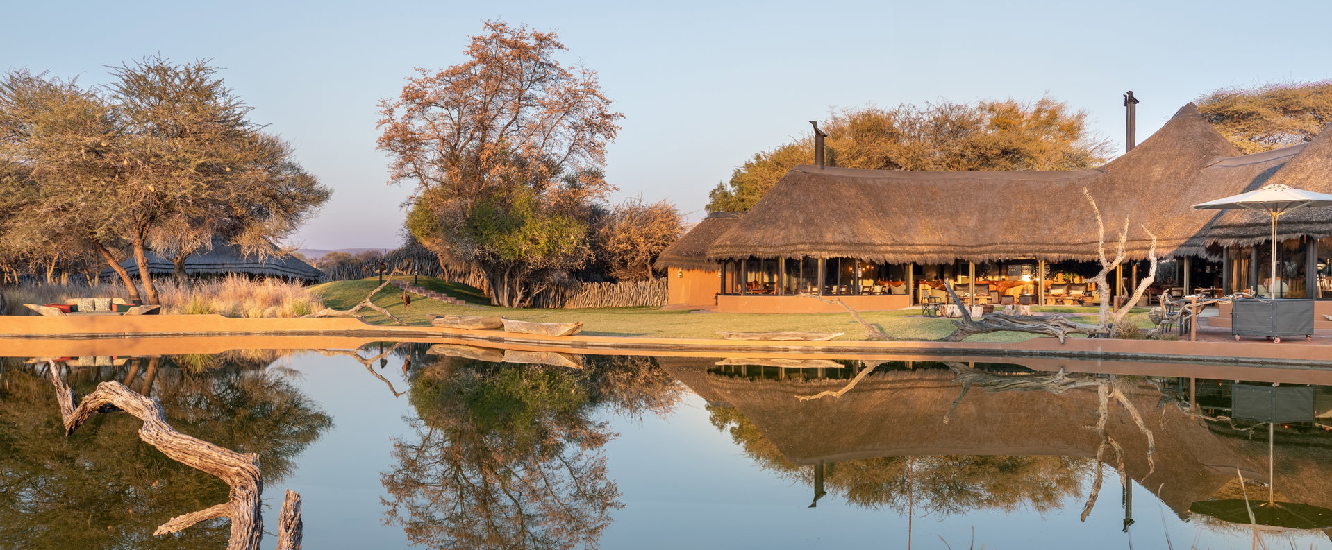 The thatched main lapa of Okonjima Luxury Bush Camp reflected in its waterhole