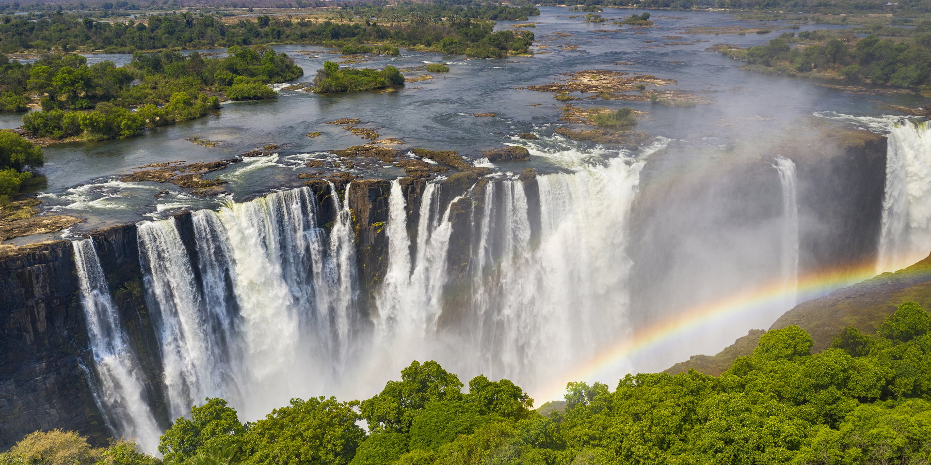A rainbow arcs over the curtain of water plunging into the Victoria Falls gorge.